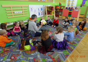 Dzieci siedzą w kole, pani bibliotekarka czyta dzieciom książkę.